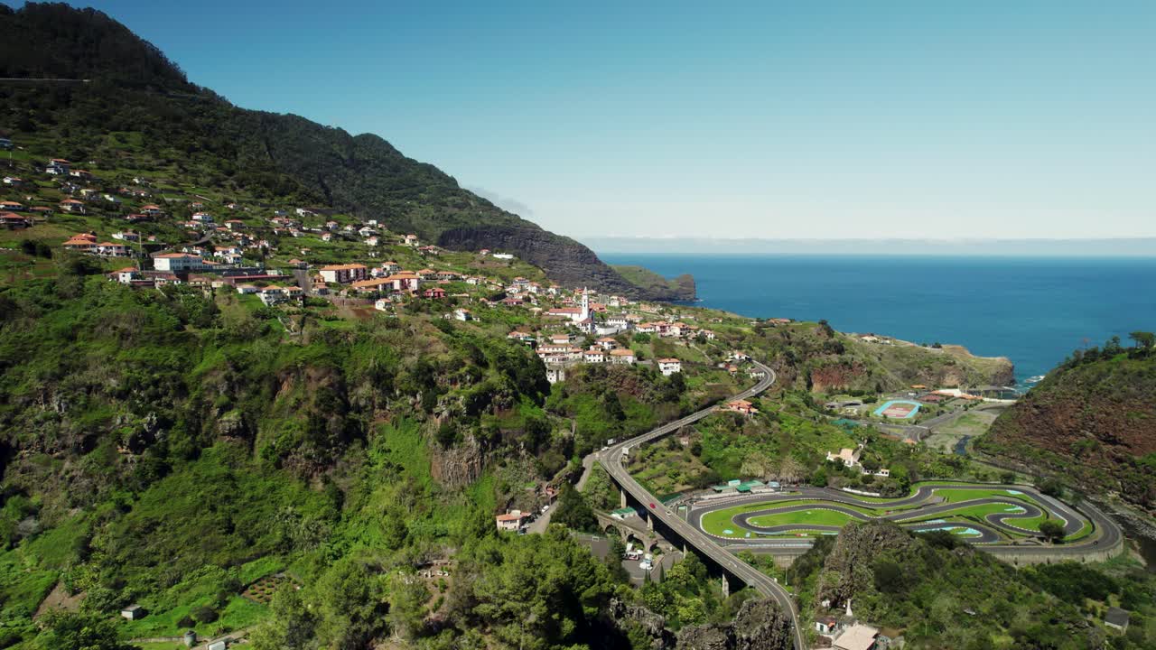 Riprese aeree con drone di un paesaggio di un villaggio di Madeira, con strada tortuosa e oceano sullo sfondo.
