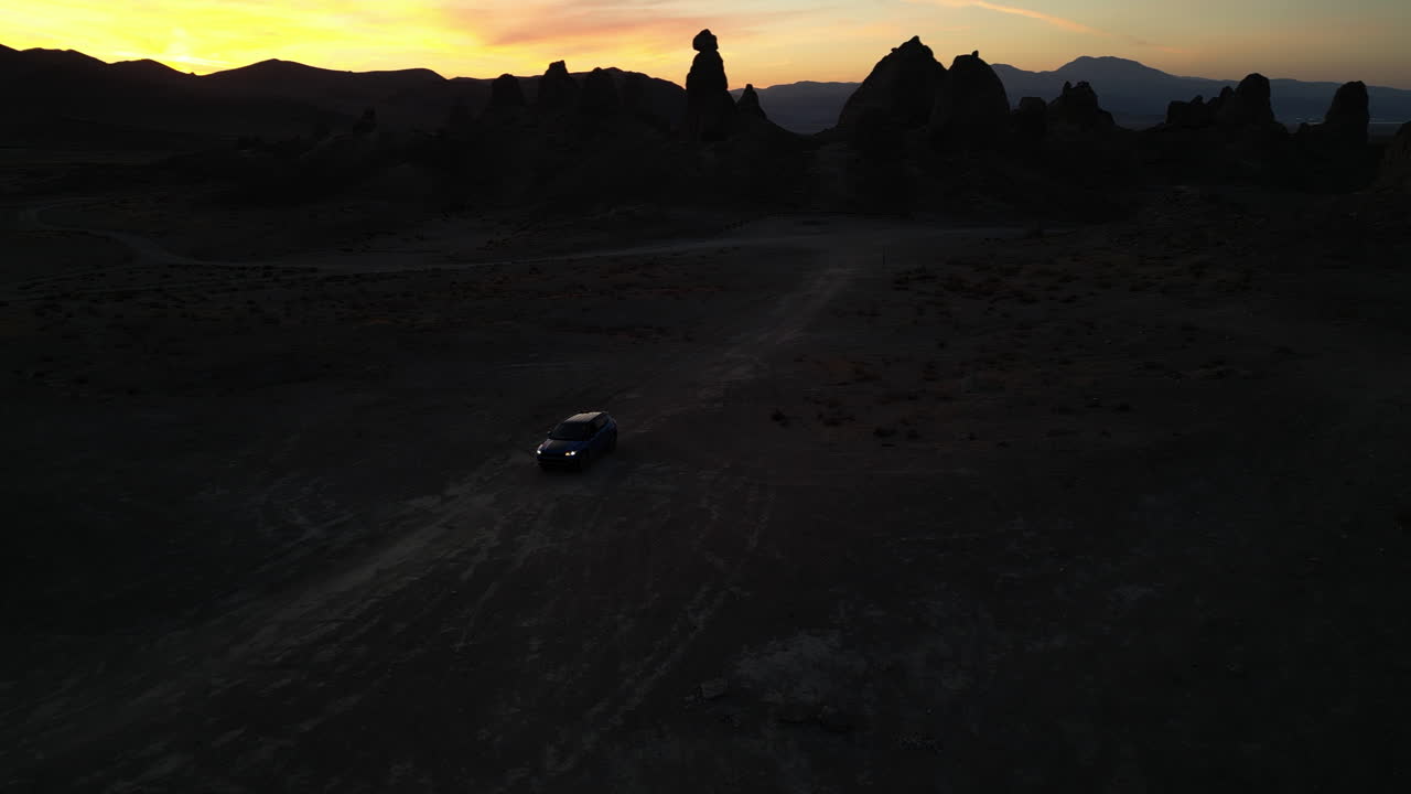 A dark sunset pan of a car driving through the desert landscape