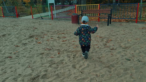 adorable caucasian toddler is on the playground in autumn. kid runs up to a bench and gets on it.