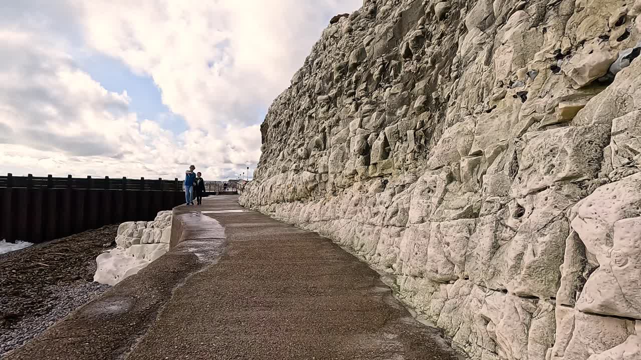 человек, идущий рядом с меловыми скалами и морской стеной