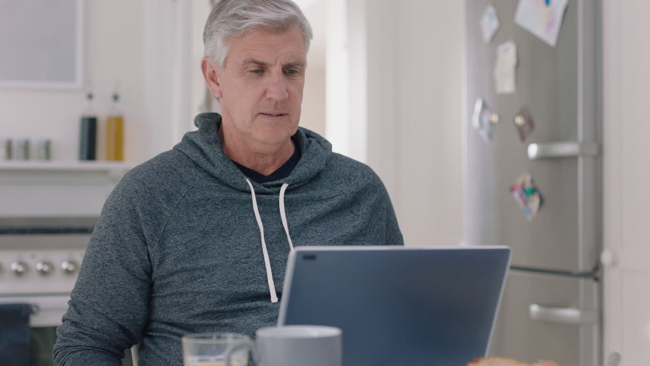 happy mature man using laptop computer at home typing messages browsing online enjoying working in morning at breakfast 4k footage