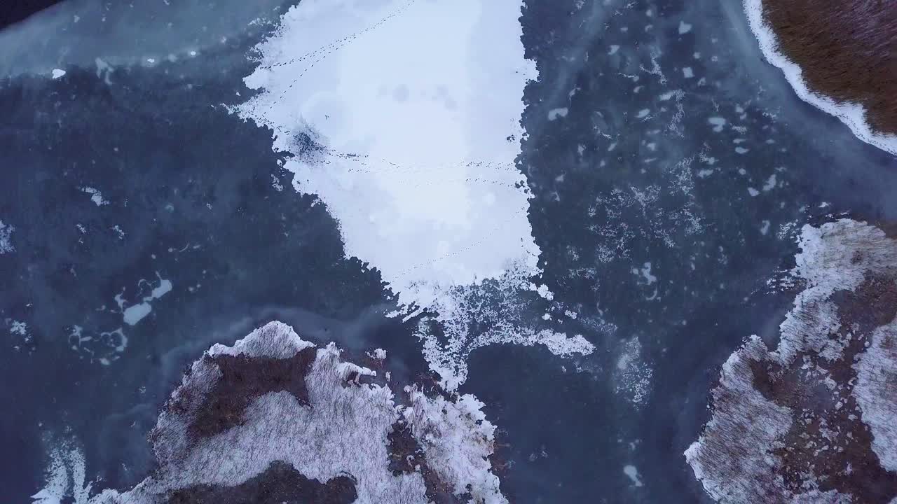 겨울 동안 얼어붙은 리파자 호수의 공중 조감도, 균열이 있는 푸른 얼음, 마른 황변 갈대 섬, 흐린 겨울날, 궤도를 도는 드론 샷
