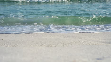 Ultra close-up shot of light waves gently crashing on a white sand beach, capturing the details of the water’s movement and foam as it meets the shore