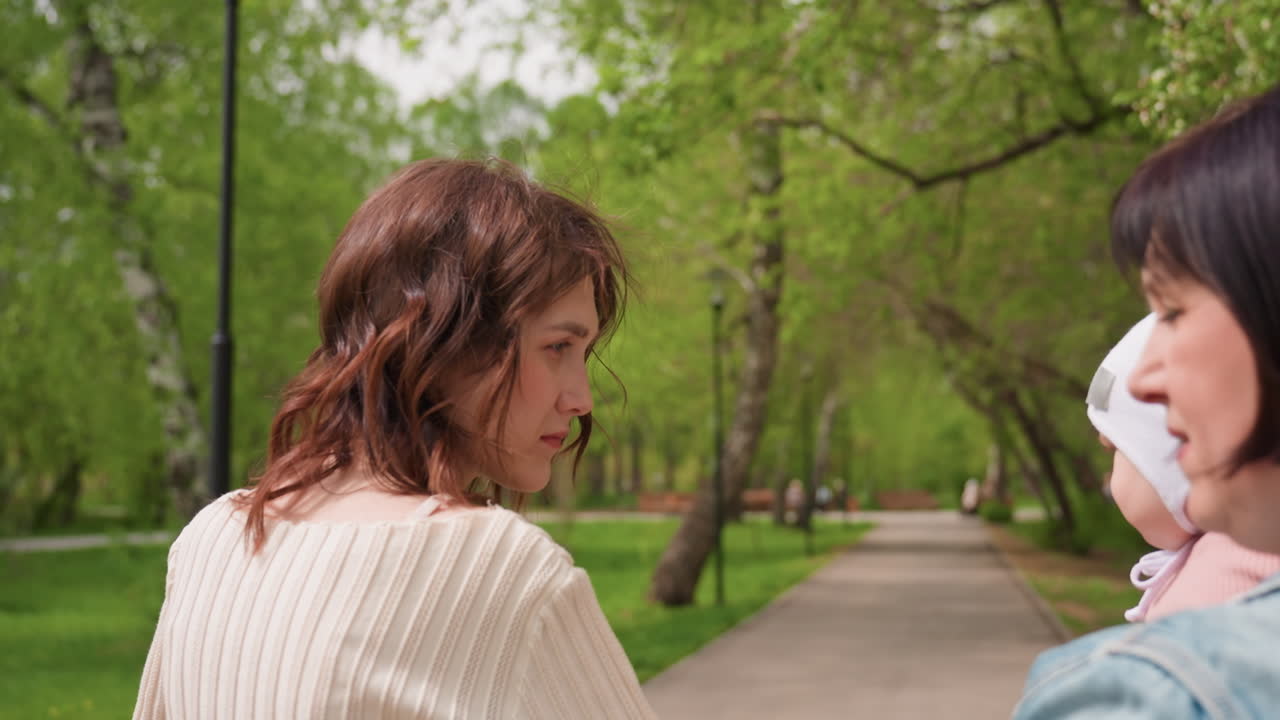 Park Mothers Exchanging Toy Beside Stroller And Wheelchair, Playful Ball, Close Conversation, Greenery Backdrop, Planning Next Steps, Caring Gestures, Supportive Circle, Spring Vibe