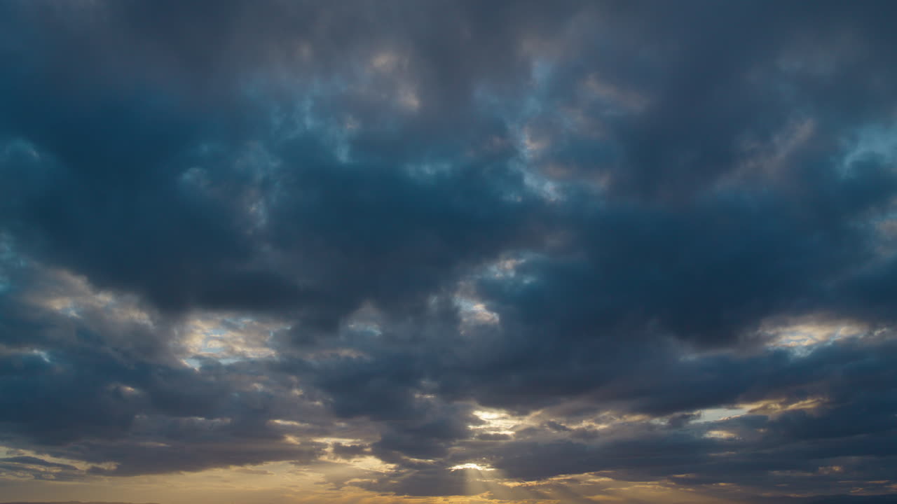paisaje de nubes al atardecer con azules y grises vívidos, resaltado por un sol dorado mirando a través