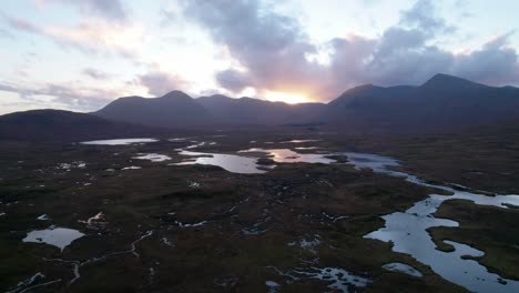 un dron se eleva lentamente para revelar un paisaje de humedales de islas y turberas rodeadas de agua dulce mirando hacia las montañas en el horizonte al atardecer