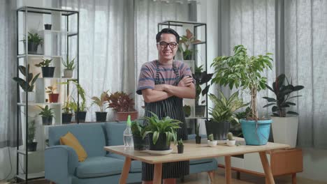 hombre asiático con plantas cruzando los brazos y sonriendo a la cámara en casa