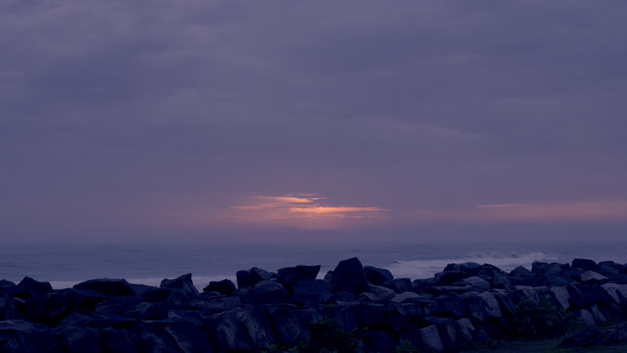 비가 오는 날 해가 지면 해변과 바위에서 보이는 구름이 가득한 태양