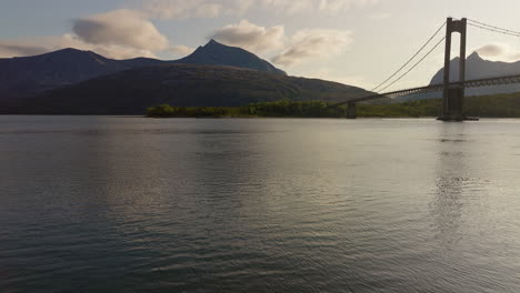 Drone-over-water-in-fjord-revealing-suspension-bridge-and-relaxing-mountain-scenery