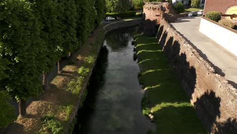 Volando-Sobre-El-Agua-Del-Canal-A-Lo-Largo-De-La-Pared-De-Bastioni-Balestrieri-En-Soncino,-Italia