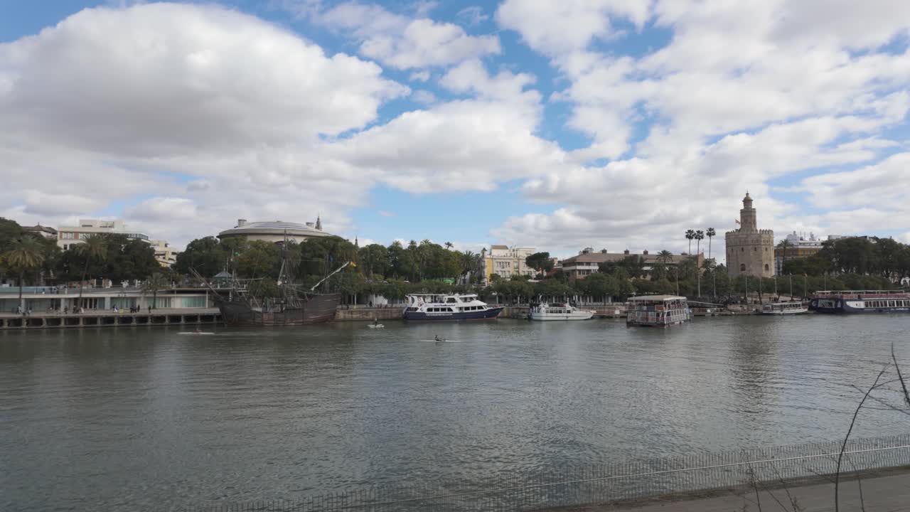 Panoramic view of Torre del Oro reflecting on Guadalquivir river with boats moored and cloudy sky in Seville, Andalusia, Spain