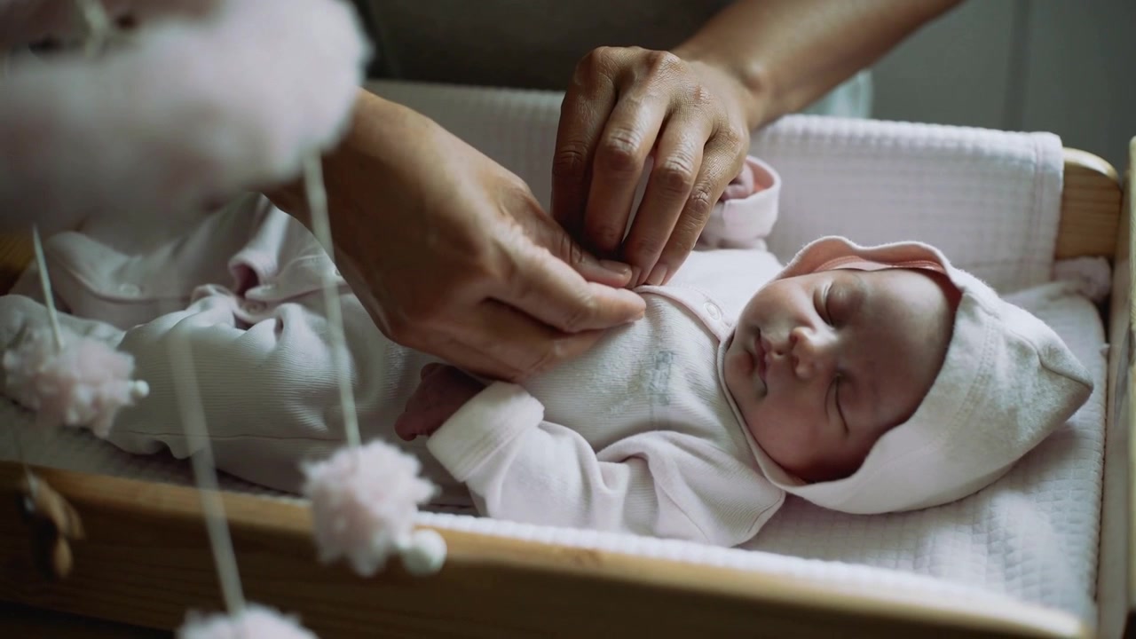 Mani di un assistente che allacciano i bottoni automatici anteriori di una tutina rosa con cappuccio nella culla della nursery per il calore