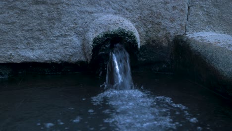 closeup of water pouring out of granite into open pool, static establish