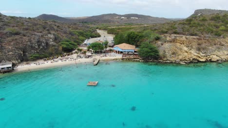 kokomo beach in curacao, clear turquoise waters with beachgoers and lush hills, aerial view