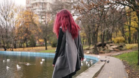 Attractive-woman-with-red-hair-walking-around-a-park-with-artificial-lake.-She-is-turning-aroung-and-smiling-to-the-camera