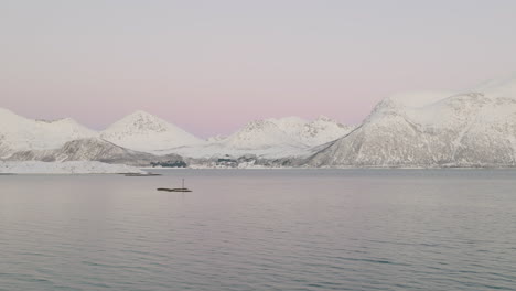 flying over a calm sea with snow-covered mountainous kvaloya island at winter in northern norway