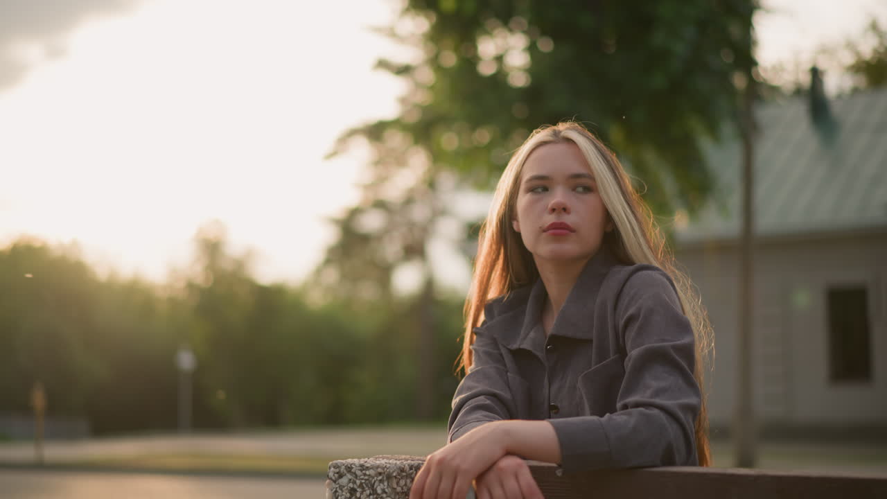 Lady in grey shirt lost in thought with hand crossed on the wood outdoors, with warm sunlight creating a serene ambience, blurred background of trees and soft lighting and building