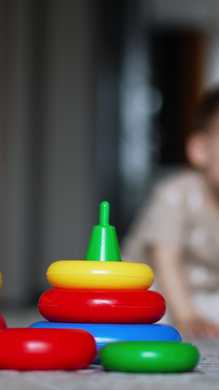 Smaller and bigger pyramid on the floor. Kid comes up to toys but then walks away. Blurred backdrop. Vertical video