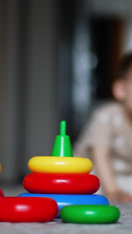 smaller and bigger pyramid on the floor. kid comes up to toys but then walks away. blurred backdrop. vertical video