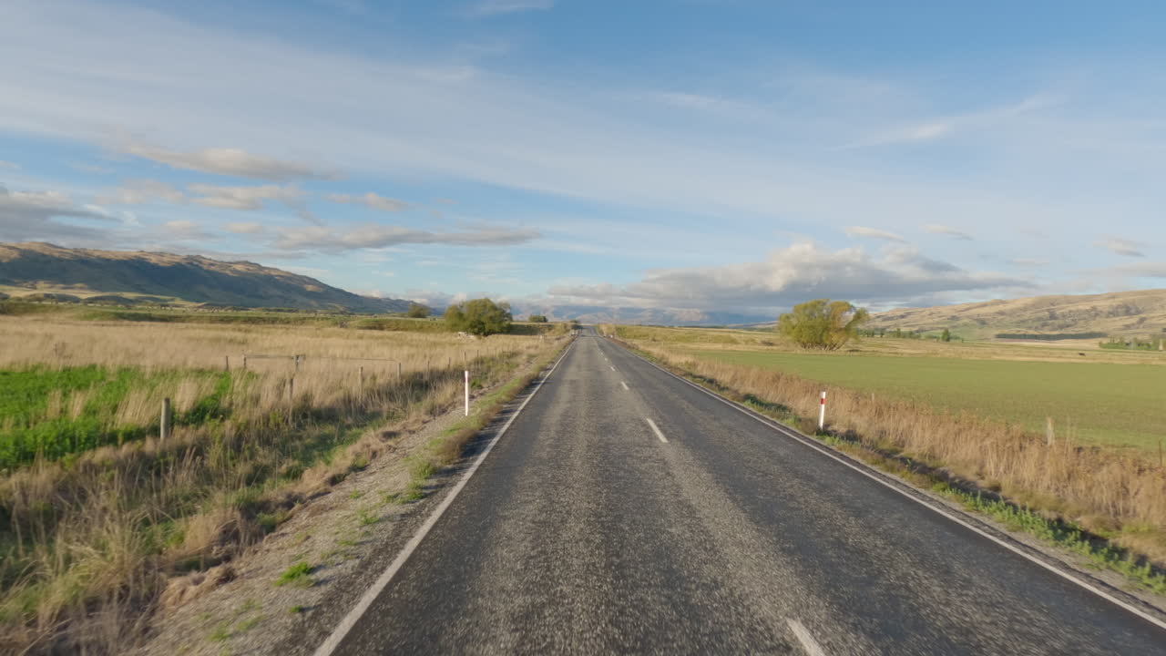 Dirigindo em estrada rural por campos em South Otago, Nova Zelândia