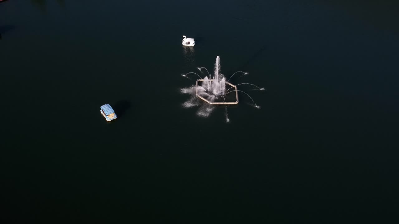 Aerial drone shot flying forward over a lake fountain towards a swan boat