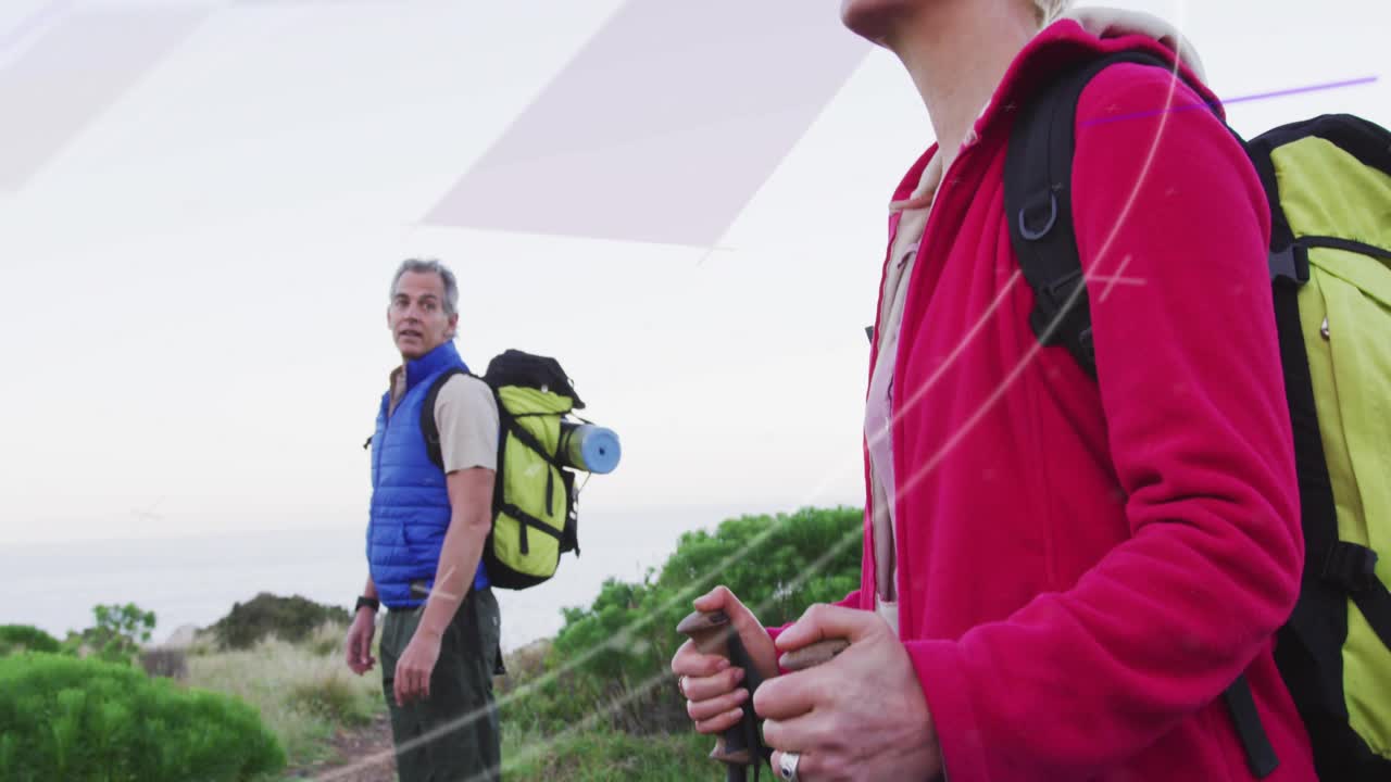 Coppia che raggiunge la cima di una collina su un sentiero costiero all'alba per mantenersi in forma, usando i bastoncini da trekking e godendosi il panorama