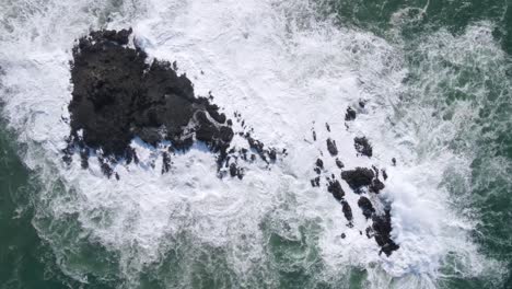 Aerial-top-down-shot-of-crashing-waves-against-rock-in-ocean,-with-white-foam