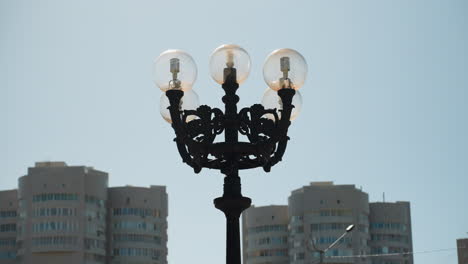 close view of an ornate street lamp with five glass bulbs, with a view of modern high-rise buildings under a clear blue sky