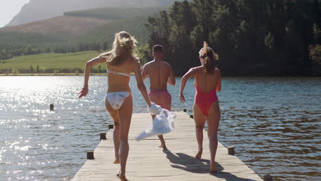 happy-friends-jumping-off-jetty-in-lake-running-undressing--at-sunset-having-fun-splashing-in-water-enjoying-freedom-sharing-summer-vacation-adventure