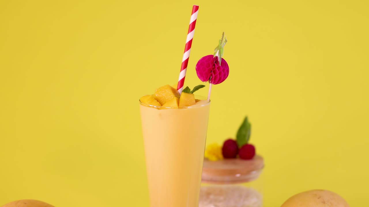 Vibrant mango smoothie glass with decorative straw, tropical garnish, and donut on bright yellow backdrop