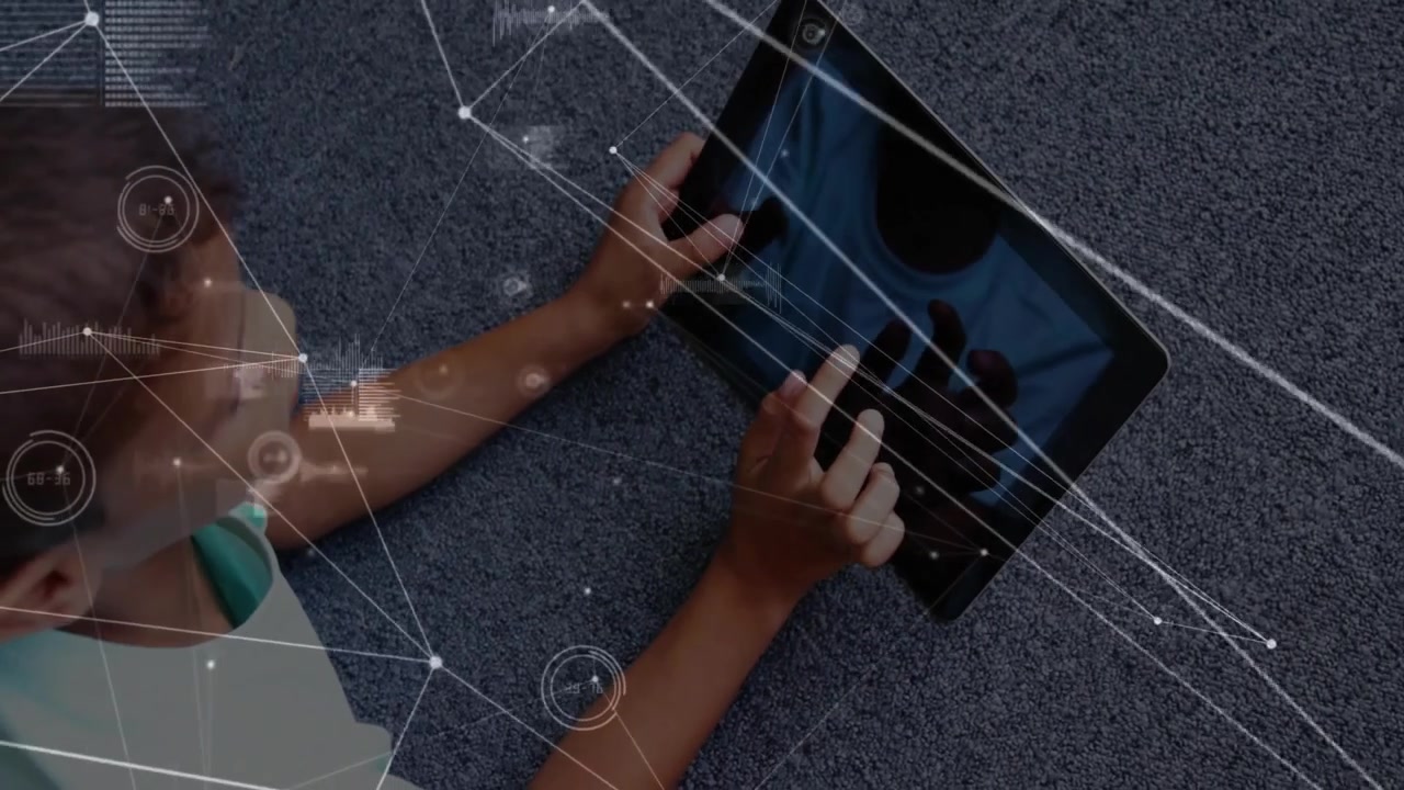 Boy lying on gray carpet tapping tablet screen for viewing network data with pulsing graphics