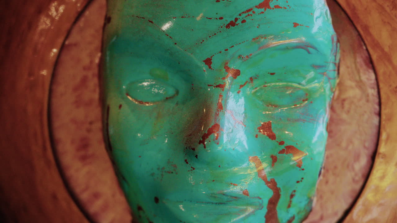 Close up of a turquoise sculpted mask with gold paint details