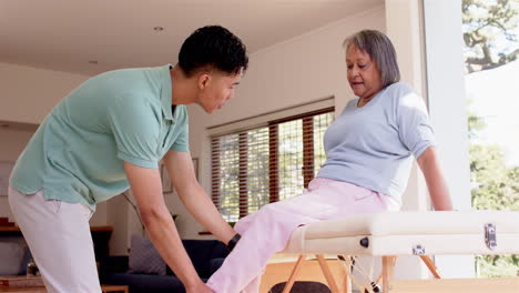physiotherapist assisting senior woman with leg exercises on treatment table indoors