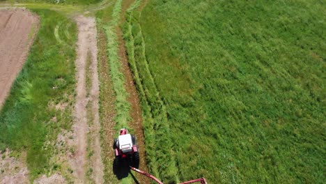 Drohnenaufnahme-Eines-Traktors,-Der-An-Einem-Sonnigen-Tag-Ein-Feld-Mit-Grünem-Heu-Erntet