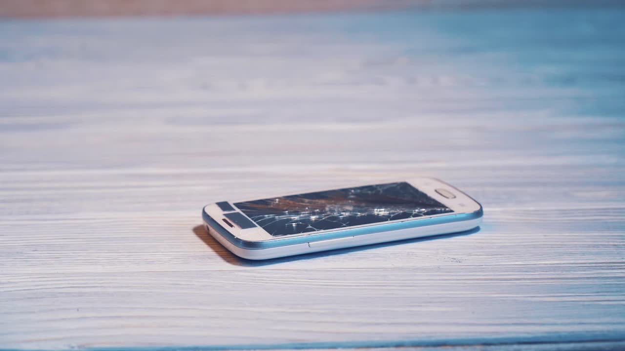 Smartphone screen cracked by hammer on the wooden background. Modern phone with large broken screen with debris broken by hammer. Close-up