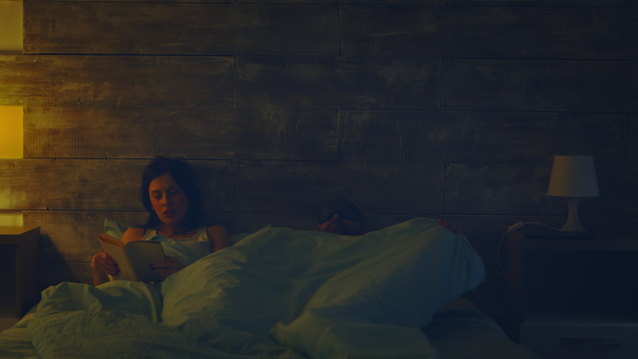 Woman reading a book in bed at night lamp