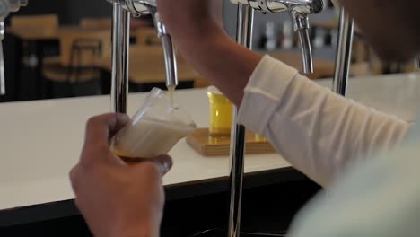 pouring of beer taster at beer tap, shot over barman's shoulder