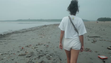 Woman-Walking-Alone-At-Tropical-Beach-With-Trash-Littered-On-Sandy-Shore