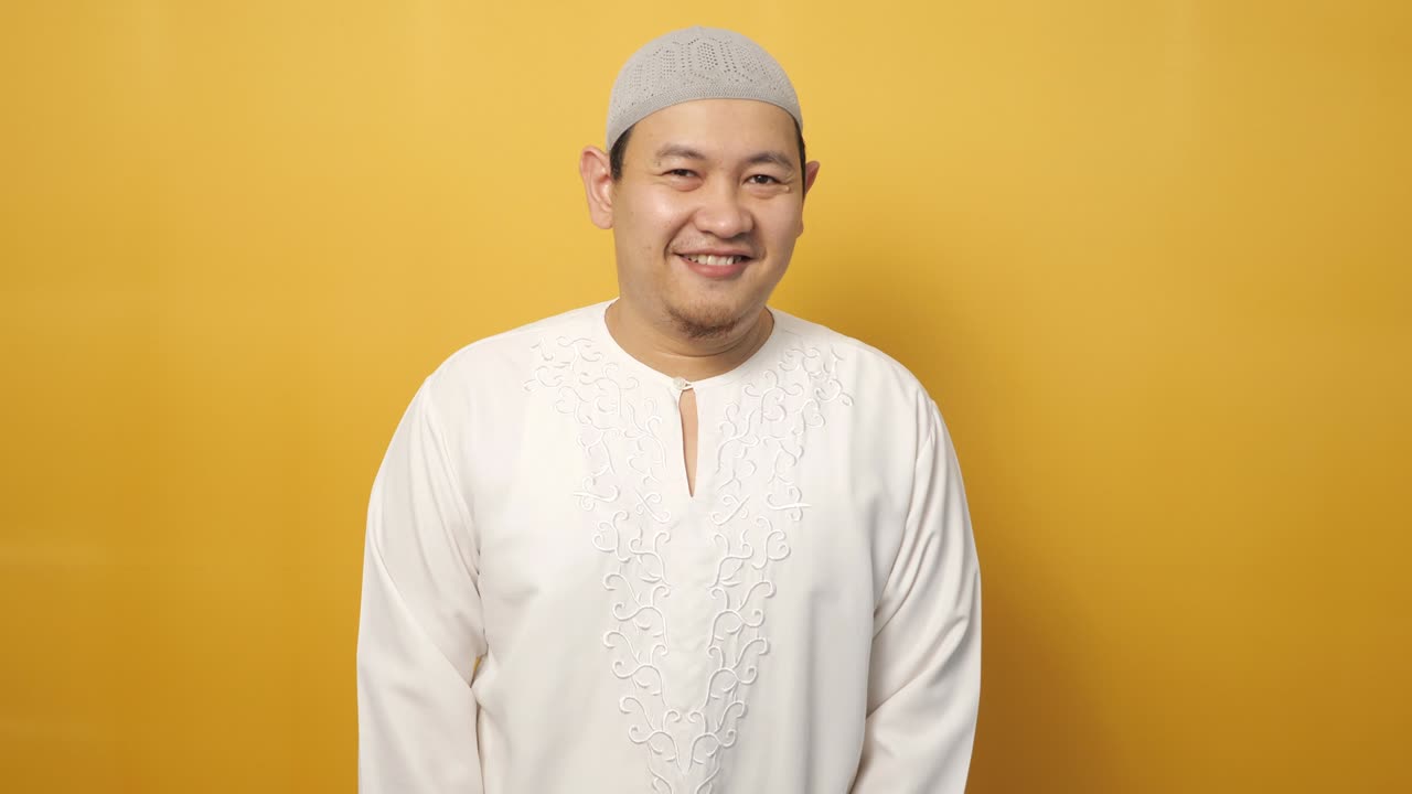 행복한 아시아 무슬림 젊은이가 노란색 배경에 미소 짓고 카메라에 포즈를 취하고 있습니다.