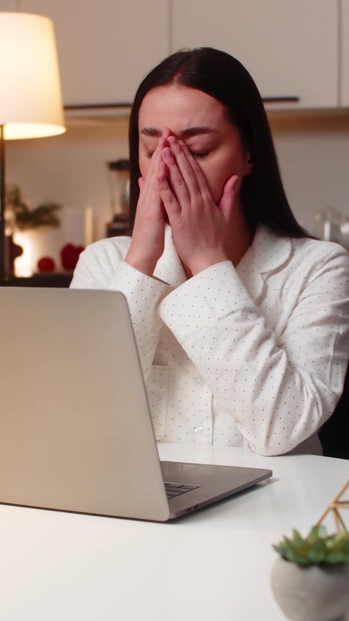 Giovane donna si massaggia le tempie per l'affaticamento visivo causato dallo schermo del laptop, si prende una pausa e poi riprende il lavoro, stanca la sera.