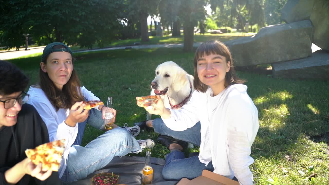 친구 들 이 피자 와 개 와 함께 공원 에서 피크닉 을 즐기고 있다