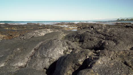 large curved lava rock in foreground with waves hitting the back of the formation