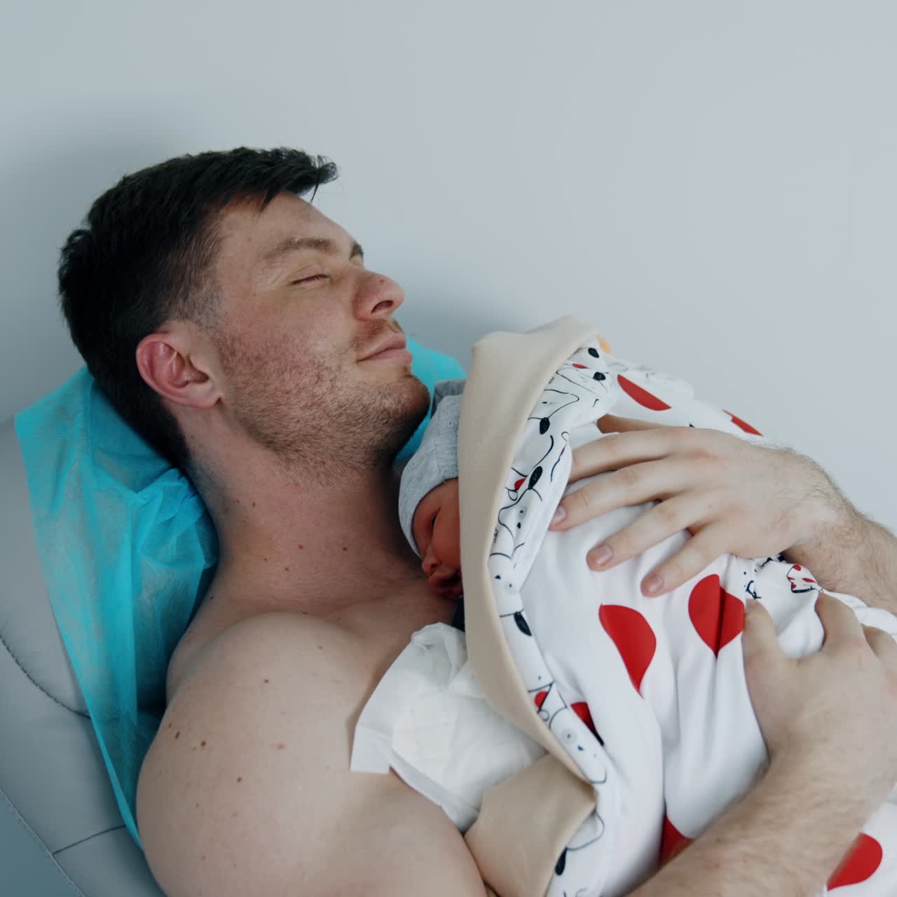 Smiling happy man holding and soothing his newborn baby on the chest. Skin to skin contact