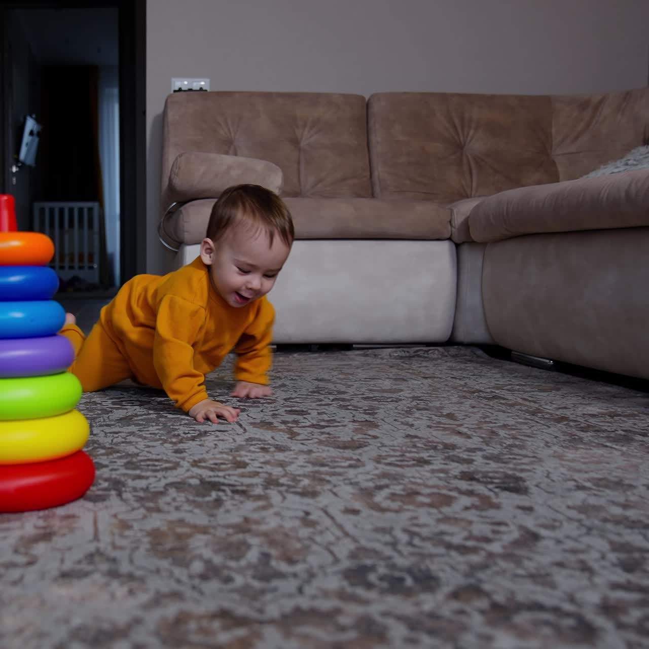 Playful cute kid crawls by the floor passing the toy pyramid. Little toddler having fun indoors