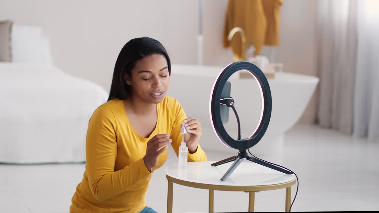 Woman applying skincare in front of ring light for online video tutorial.