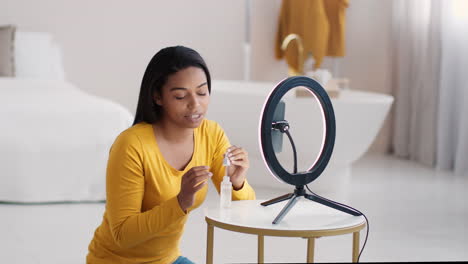 woman applying skincare in front of ring light for online video tutorial.