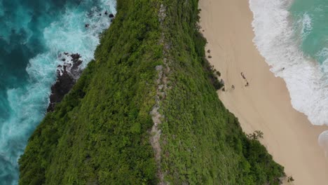 Aerial-overhead-shot-of-man-walking-down-steep-ridge-on-tropical-coast