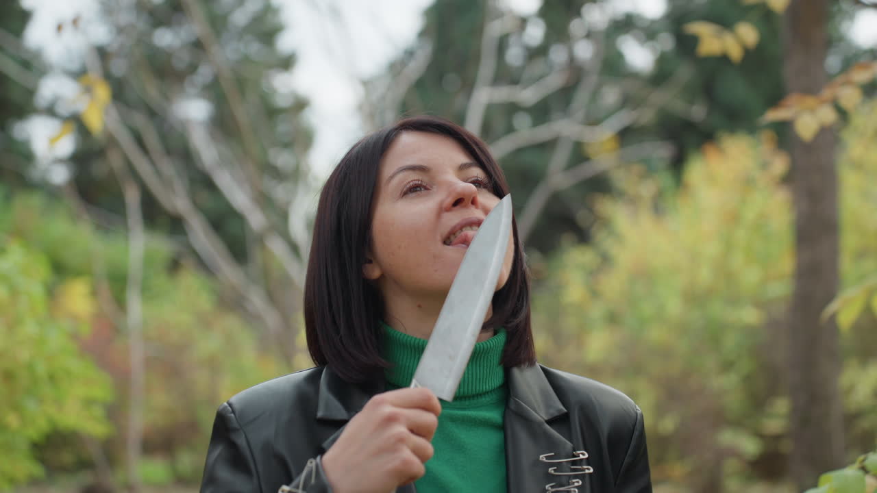 woman in leather jacket holding knife, inspecting blade near face in quiet autumn forest, green turtleneck, short brunette hair, confident contemplative expressions across sequence