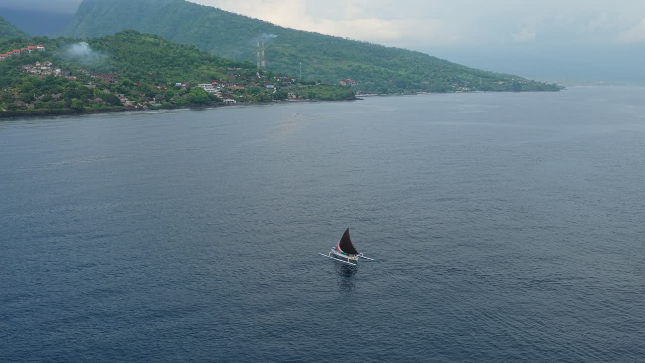 Veduta aerea di una tradizionale barca da pesca indonesiana jukung con bilancieri che naviga sul mare tranquillo lungo la costa di Amed, Bali.