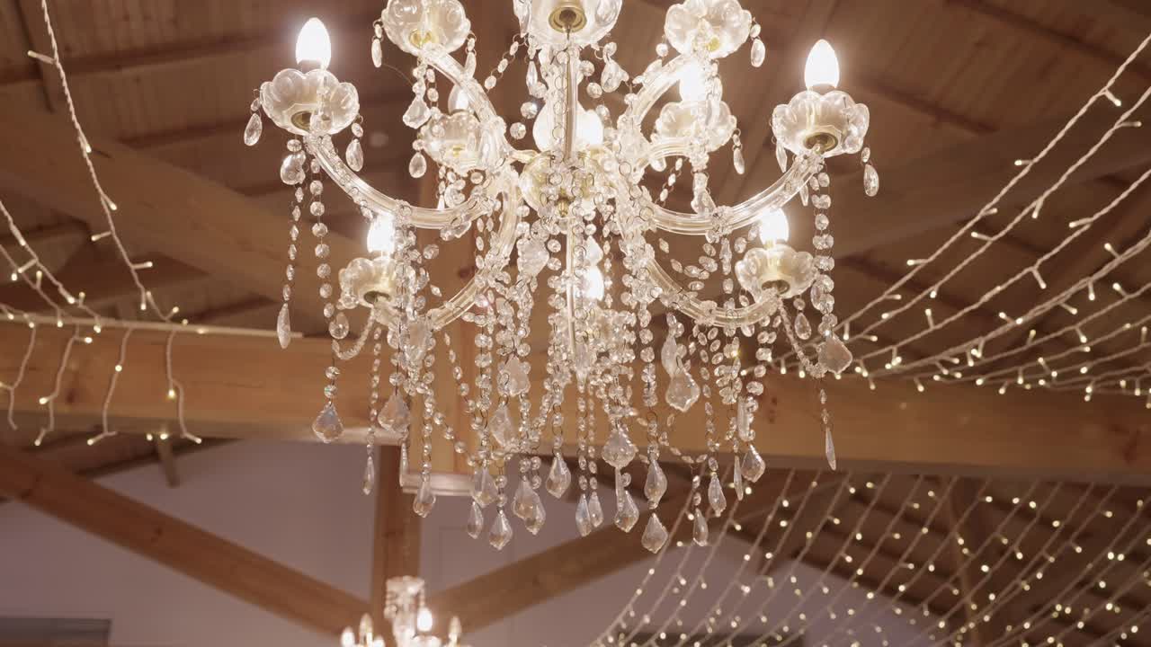 Lámpara de araña de lujo con gotas de cristal brillando entre luces de hadas en la recepción de una boda